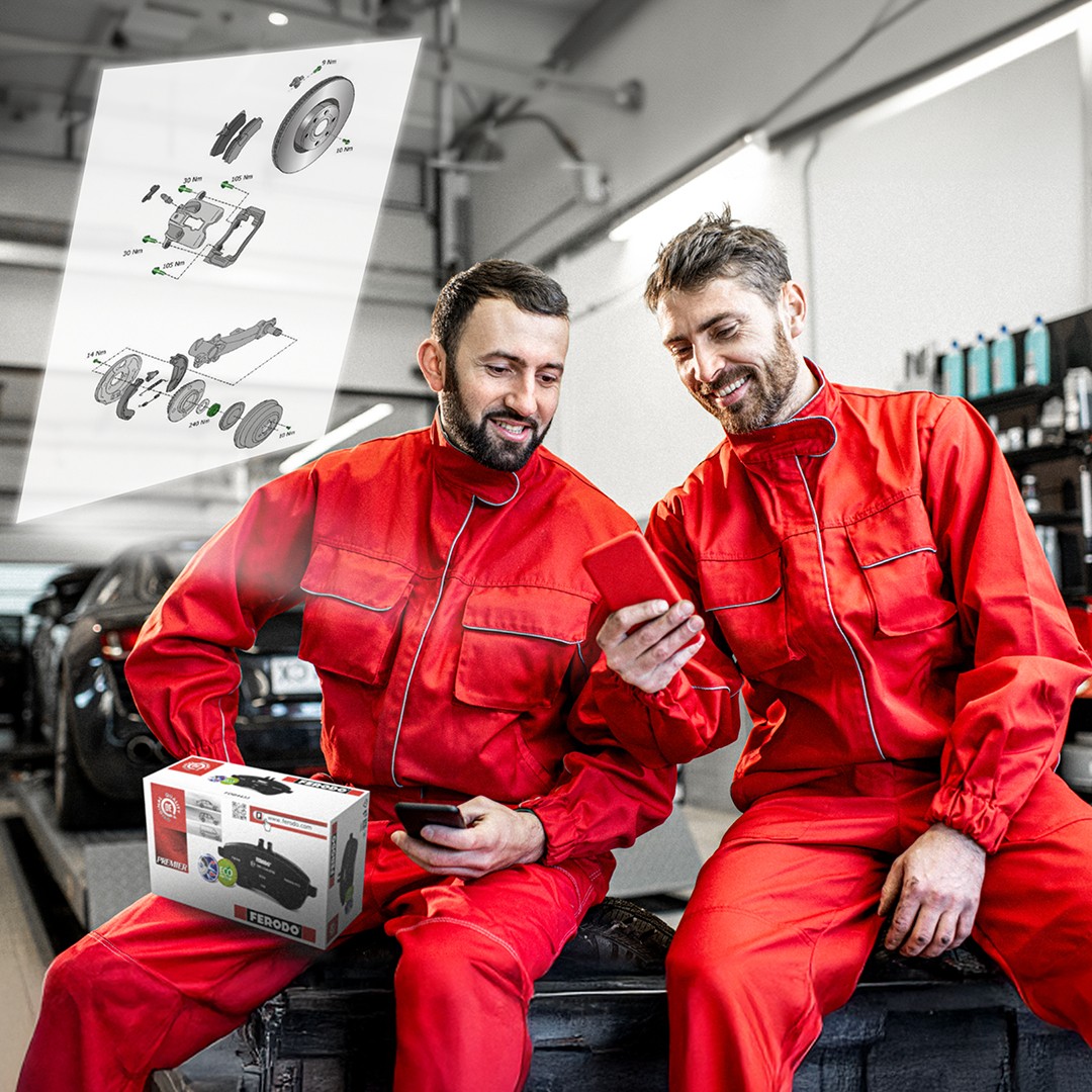 Two automotive mechanics in a workshop examining detailed Ferodo technical drawings accessed by scanning a Ferodo QR code on the product packaging