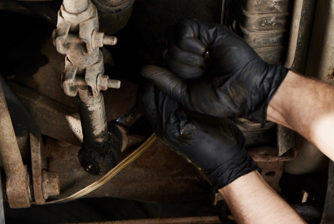 Mechanic-Working-On-Suspension-System A mechanic's hand adjusting a strut on the bottom of a vehicle.