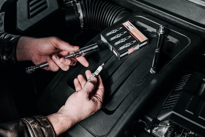 mechanic-holding-champion-spark-plug-and-socket-wrench A hand holding a spark plug and a tool