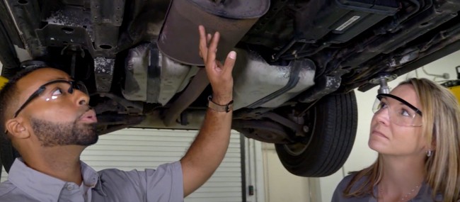 how-to-perform-exhaust-system-inspection-1 Auto technicians examining exhaust system under a vehicle lifted up at the shop